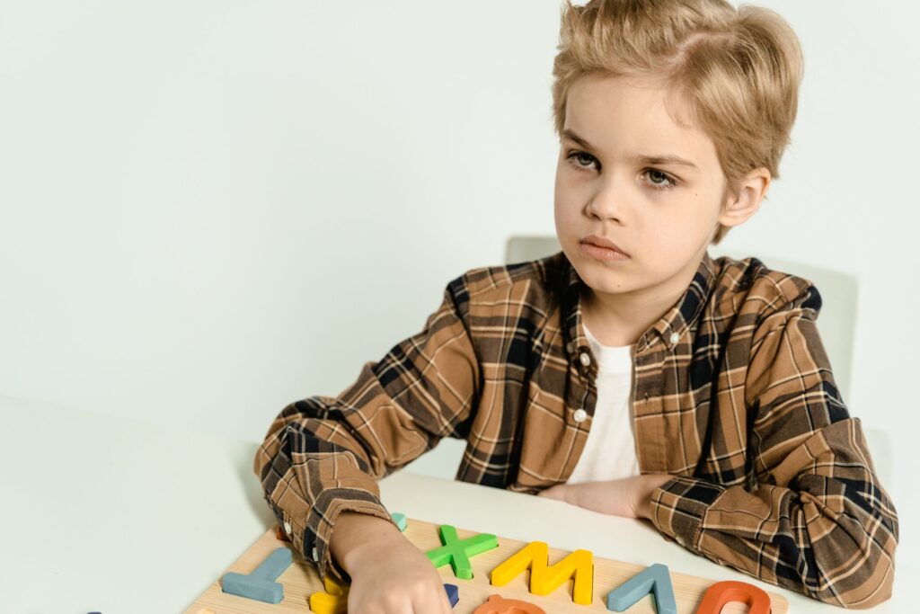 A young boy in a plaid shirt playing with colorful letters on a table indoors.
