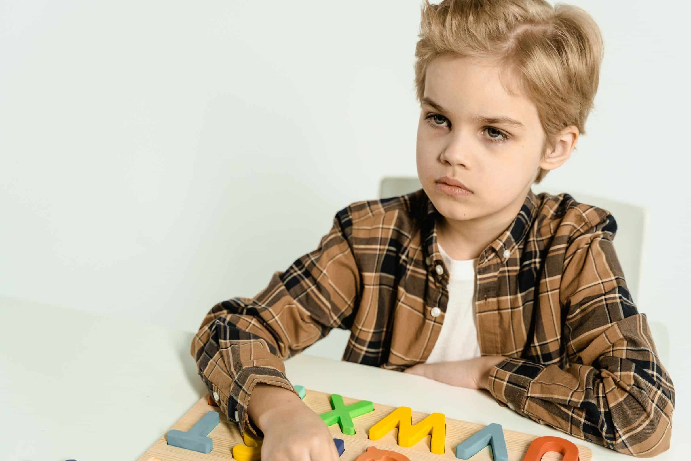 A young boy in a plaid shirt playing with colorful letters on a table indoors.